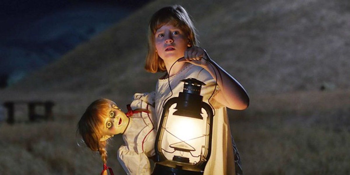 A girl holds a lantern and the infamous killer doll in Annabelle Creation