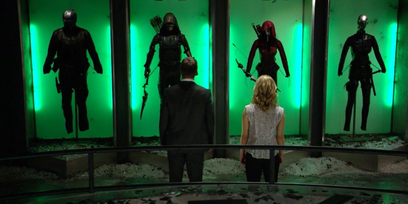 Oliver Queen and Felicity standing in The Arrow Bunker. They are standing in front of Spartan, Green Arrow, Speedy and Black Canary suits