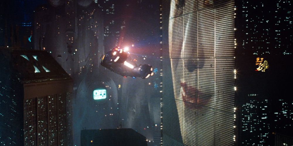 A picture of the classic scene in Blade Runner of the spinner car flying by the building advertisement is shown.