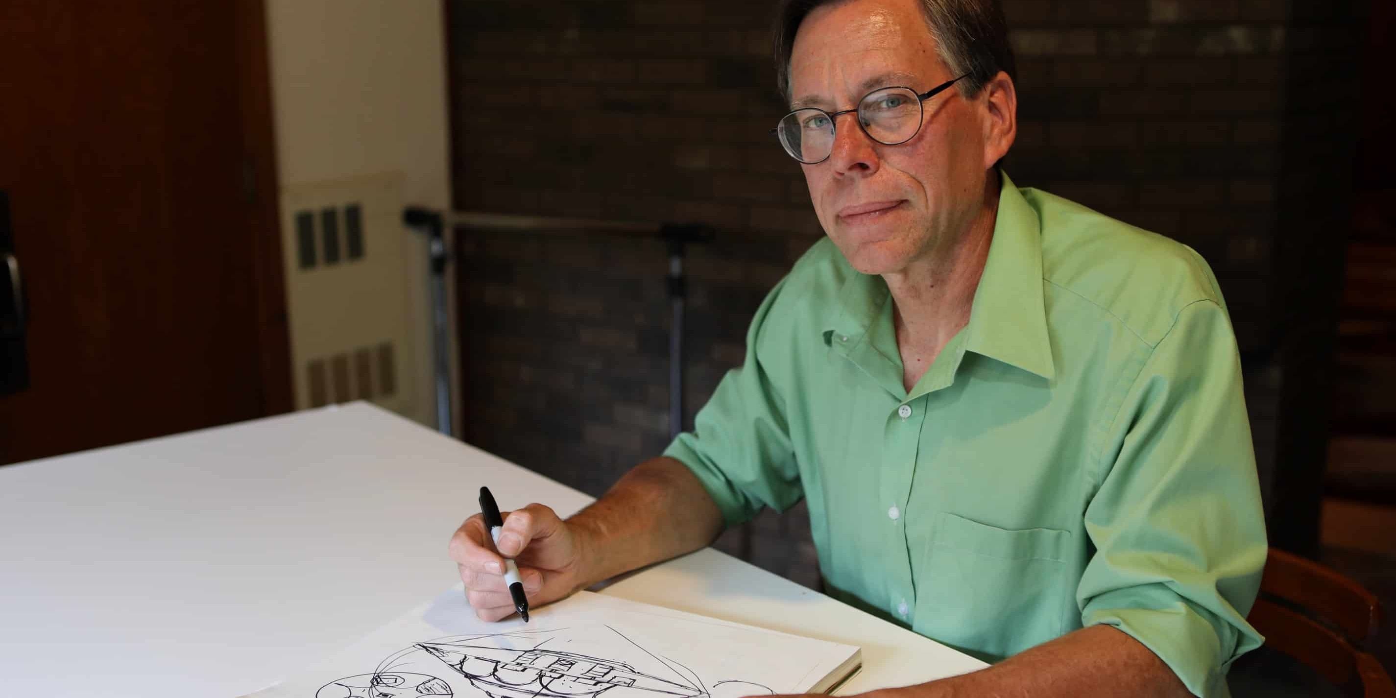 Bob Lazar sits in front of a table with a marker in his hand