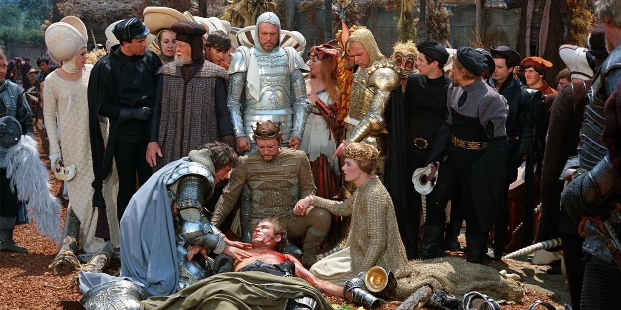 Main characters gathered around a wounded man in Camelot
