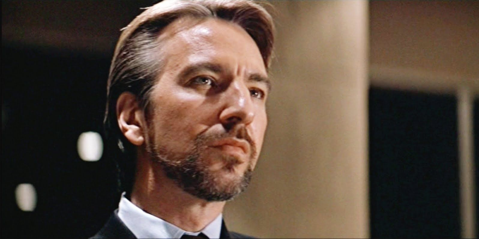 Alan Rickman as Hans Gruber with a serious expression as he looks at someone off camera in Die Hard