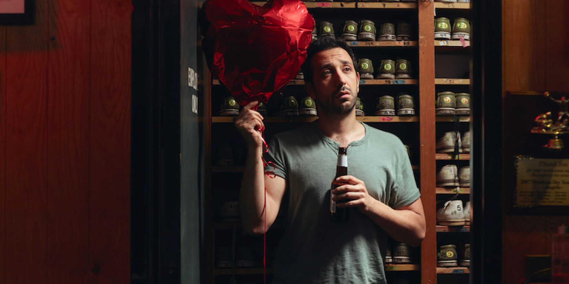 Edgar holds a balloon and a drink at the shoe closet in a bowling alley in Youre The Worst