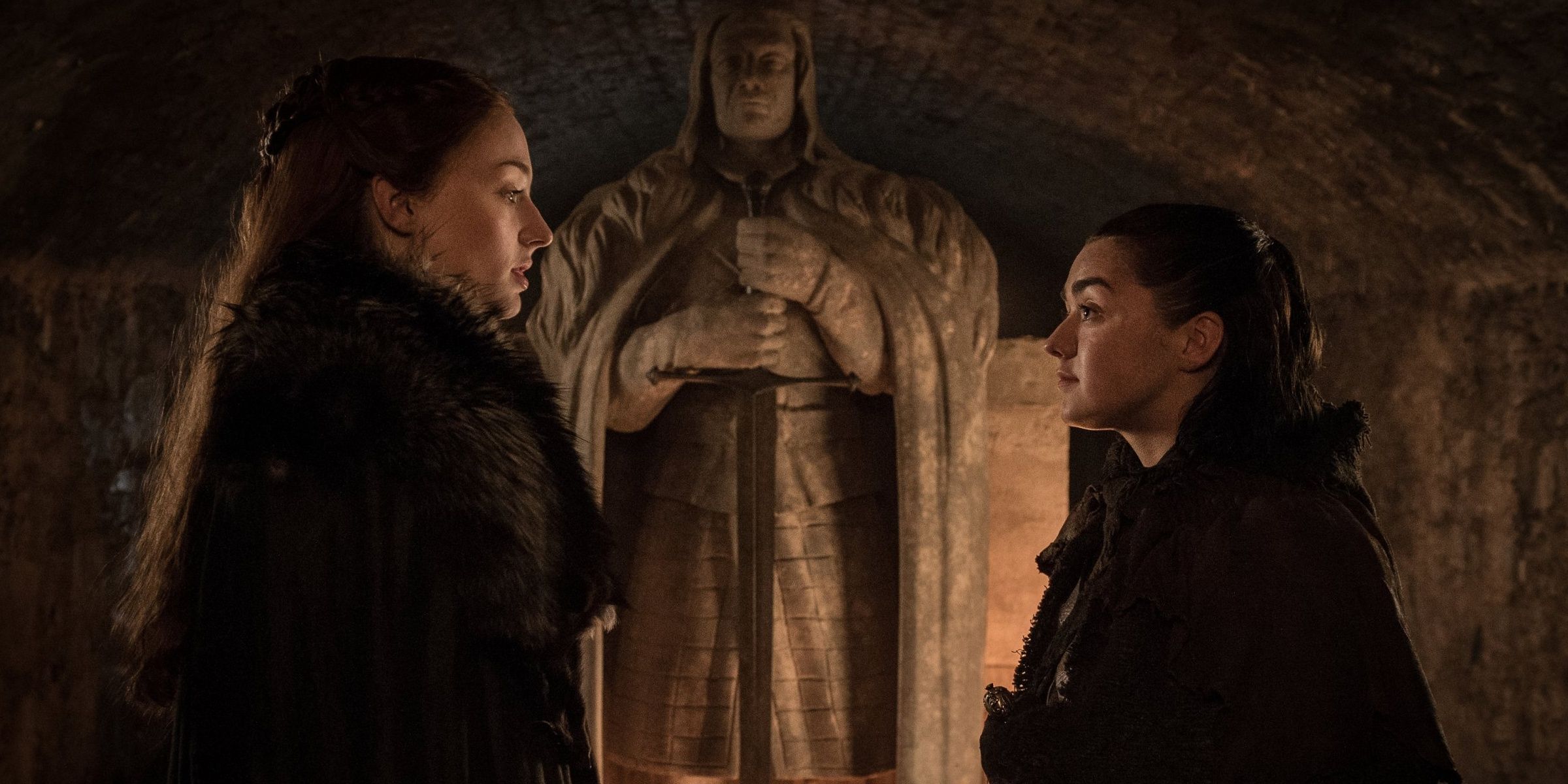 Sansa and Arya talk in front of their father's statue in Winterfell in Game of Thrones 