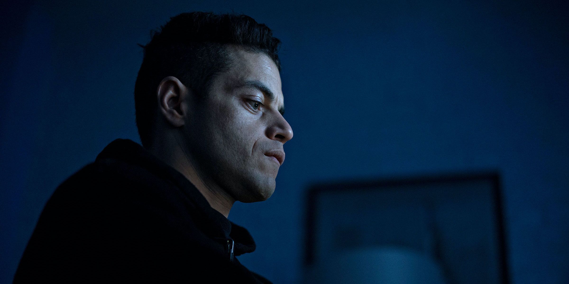 Rami Malek in Mr. Robot on a dark background, looking at his computer.