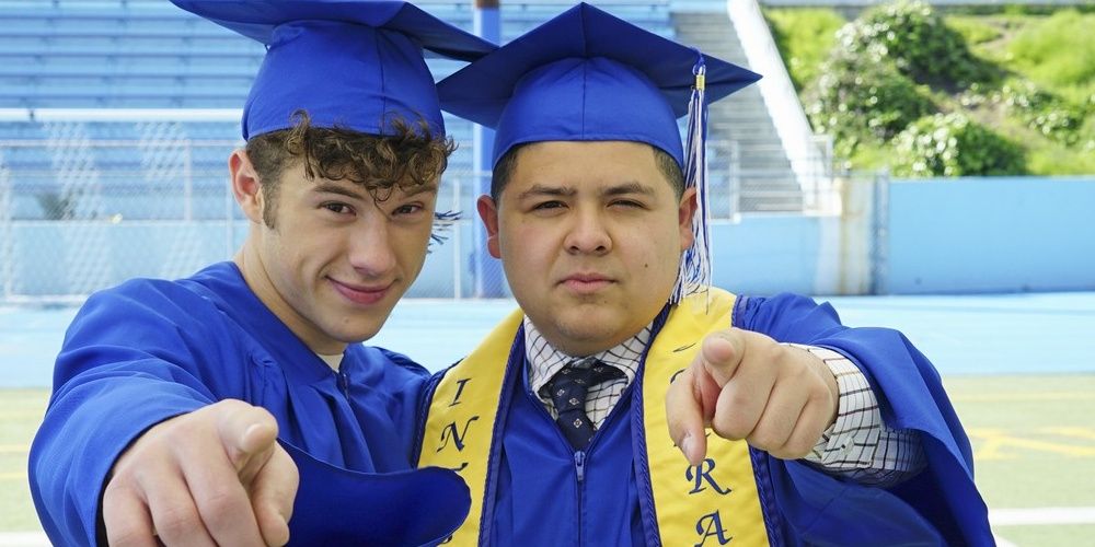 Luke and Manny pointing at the camera with their graduation robes in Modern Family