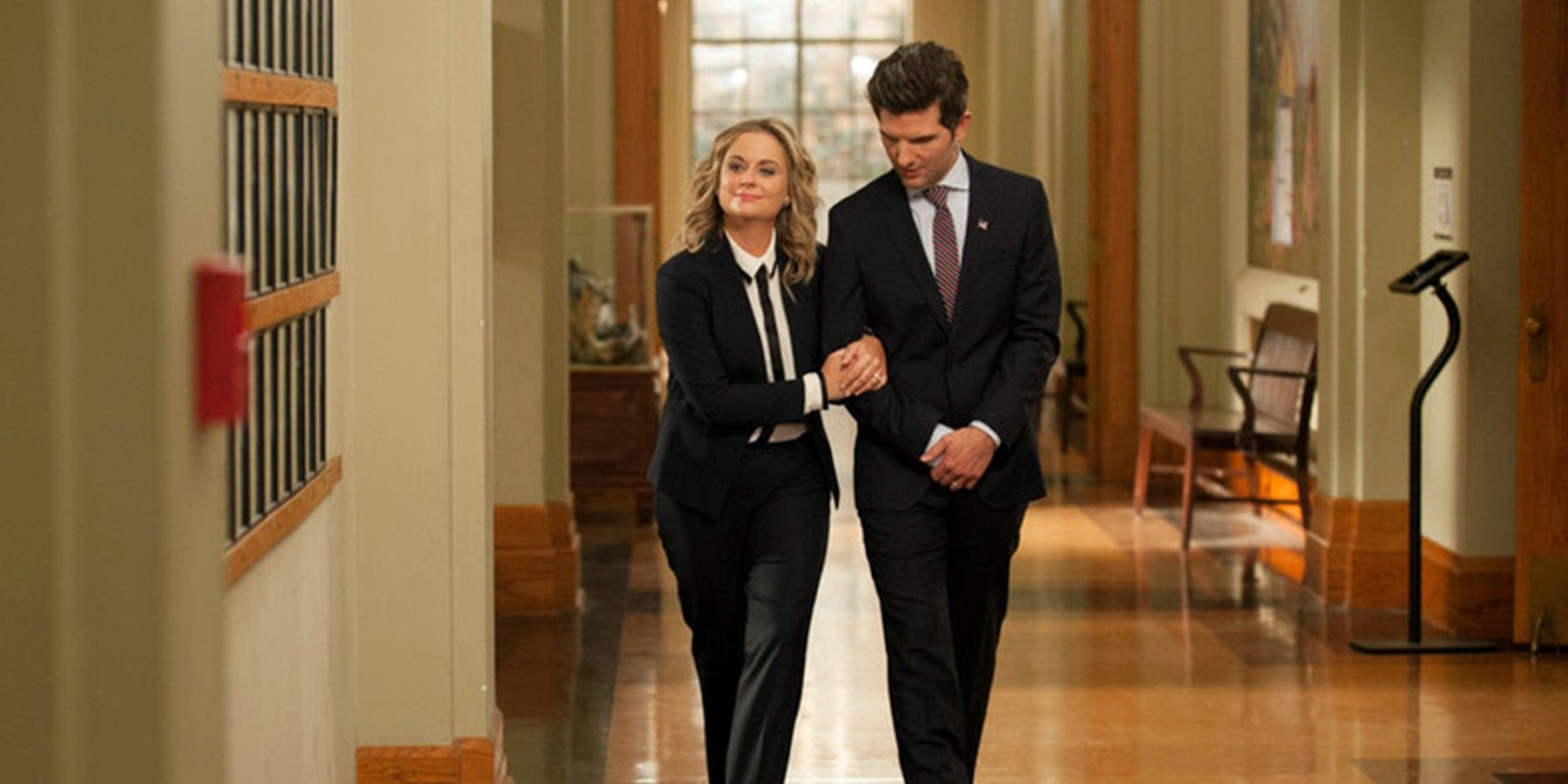 Leslie Knope (Amy Poehler) e Ben Wyatt (Adam Scott) de braços dados caminhando pelo corredor