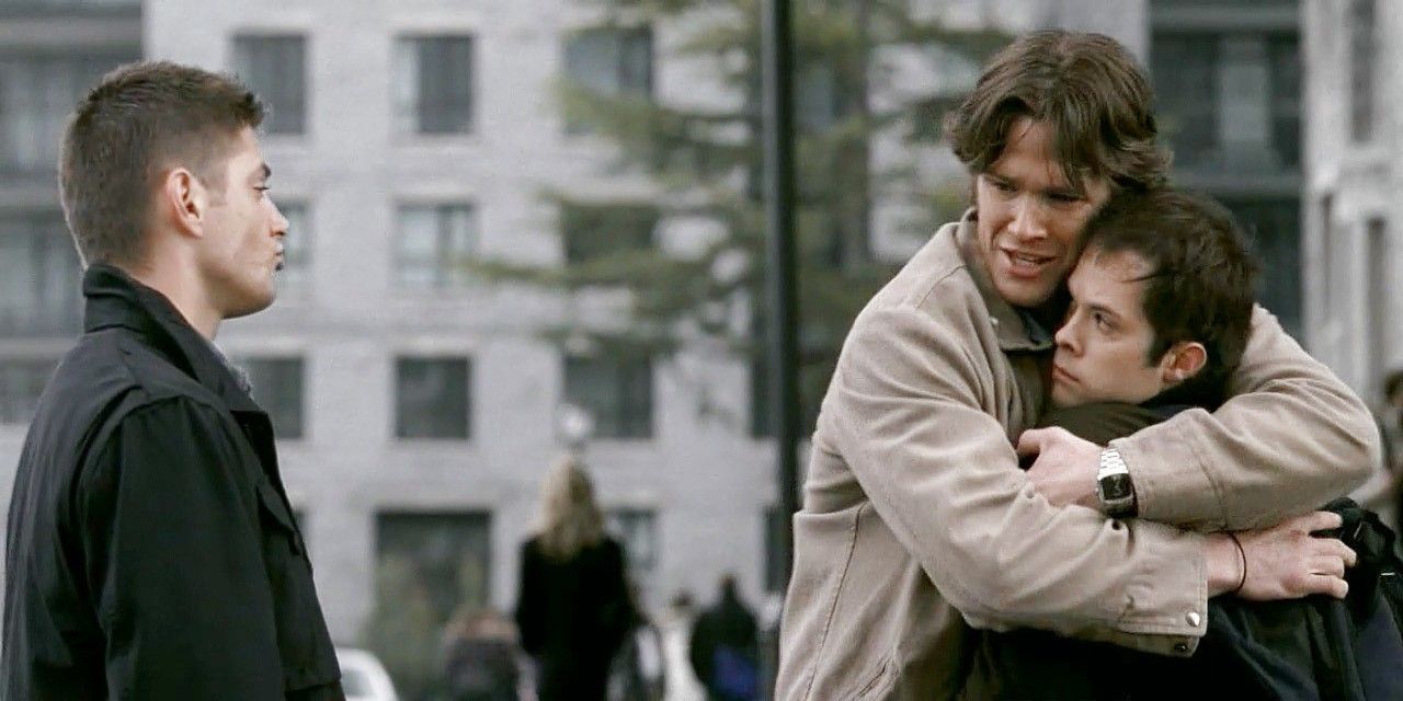 Sam hugs a young man while Dean watches in Supernatural