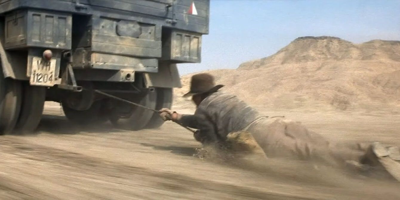 Indy hangs off a moving truck in Raiders of the Lost Ark.