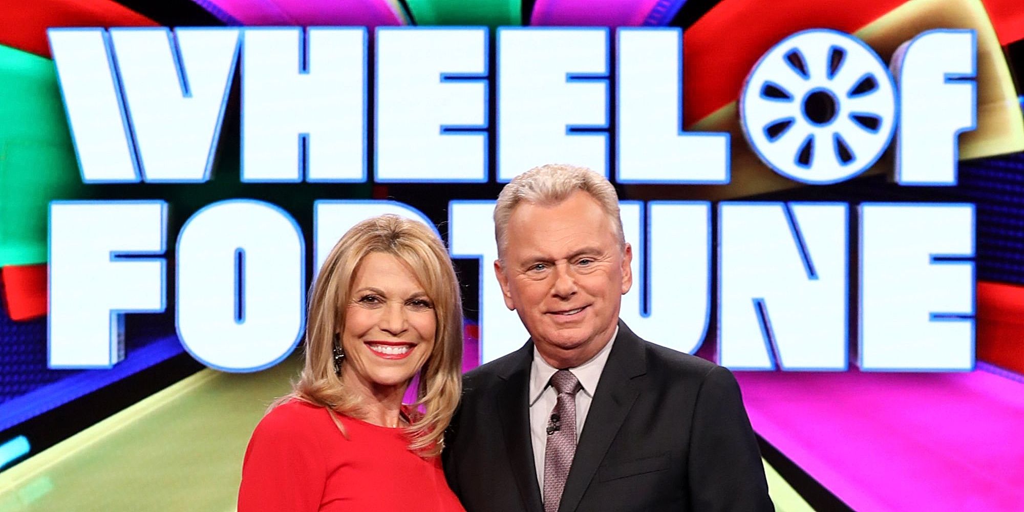 Vanna White and Pat Sajack amiling in front of the Wheel of Fortune sign.