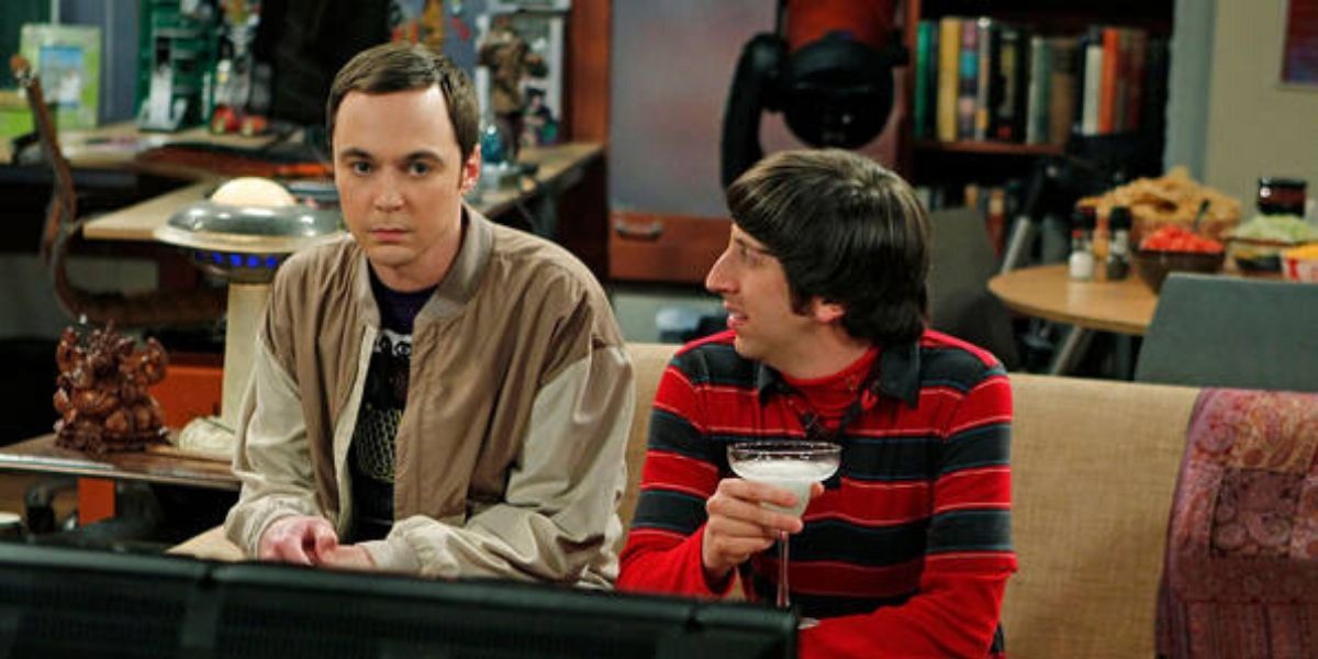 Sheldon wearing a beige jacket sitting next to Howard who is holding a margherita 