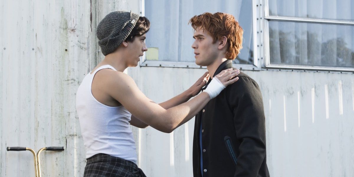 Jughead face to face with Archer with hands on Archie's shoulders