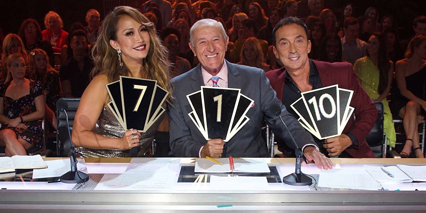 Carrie Ann, Len, and Bruno smiling and holding the judges handle in Dancing with the Stars