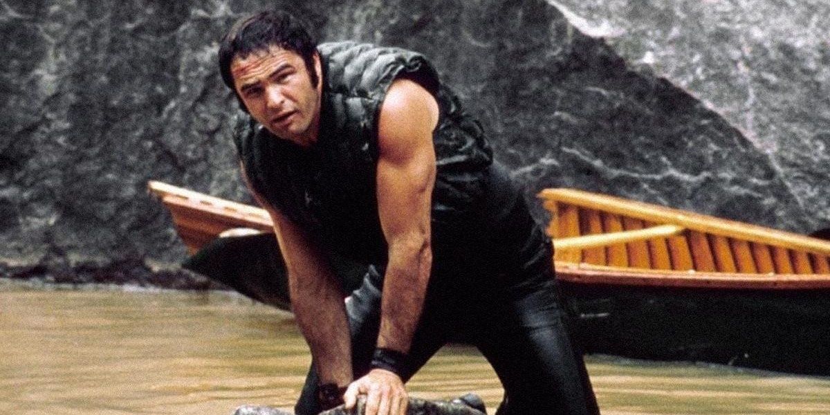 Burt Reynolds standing in front of a canoe in water in Deliverance