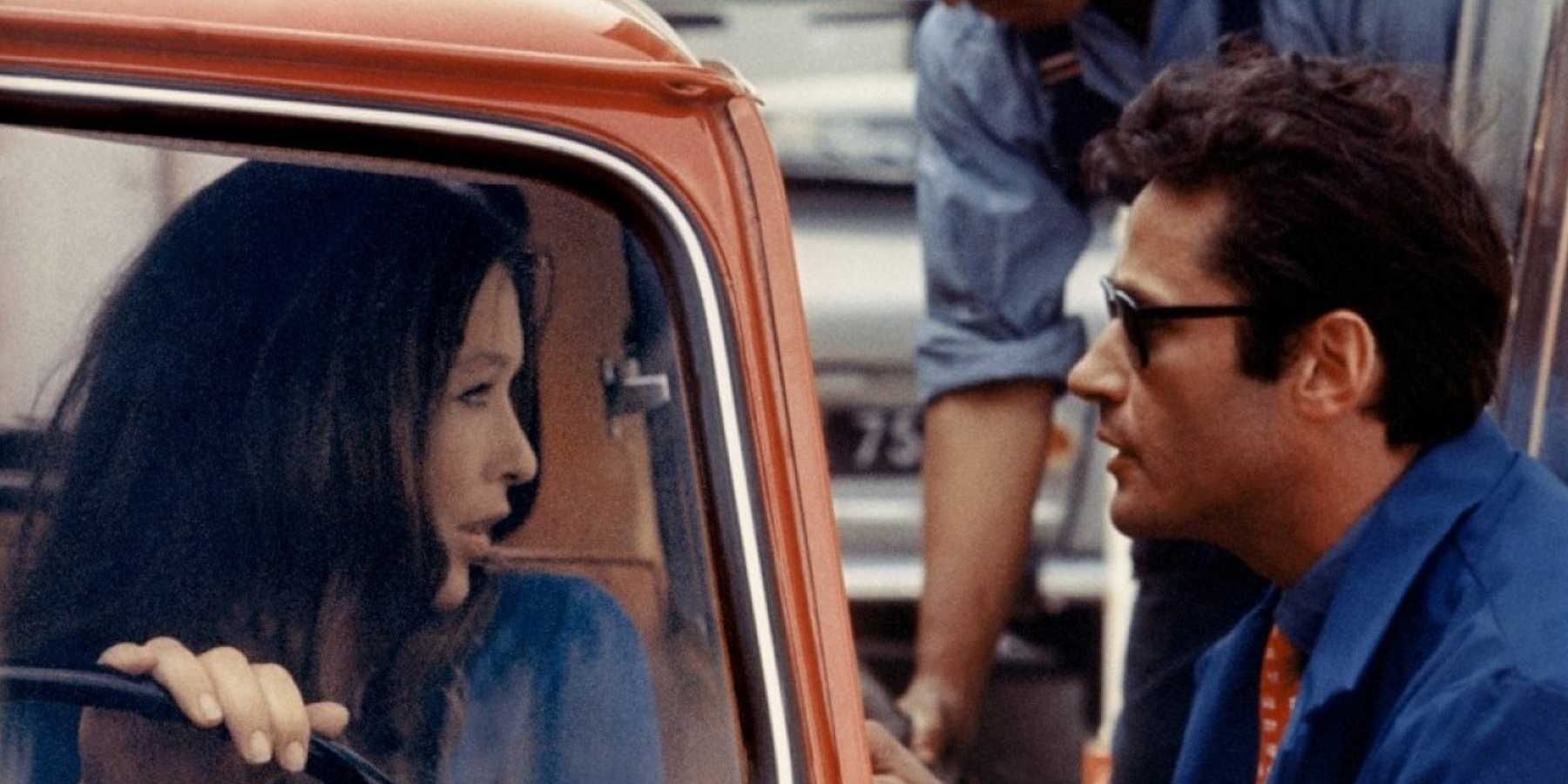 A woman holds her steering wheel as she talks to a man outside her car window in Two Or Three Things I Know About Her.