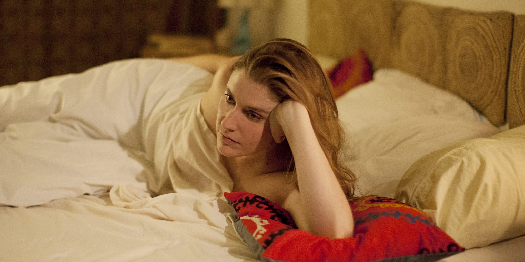 Greta Gerwig lies in bed resting her head on her hand in Eden.