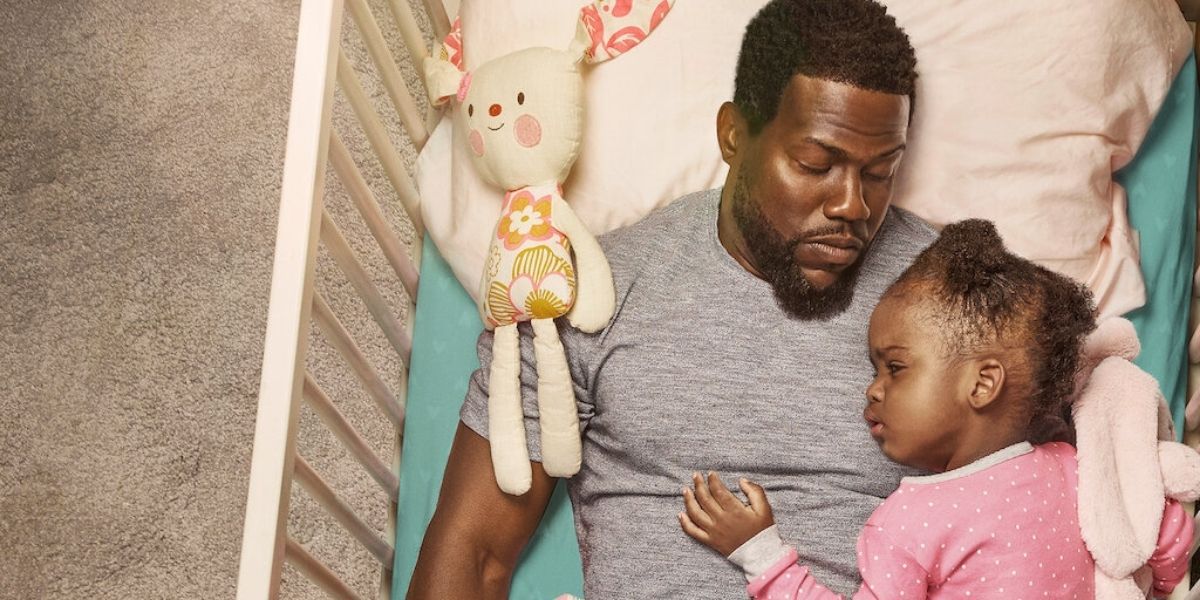 Kevin Hart lying in a crib with a small child in Fatherhood