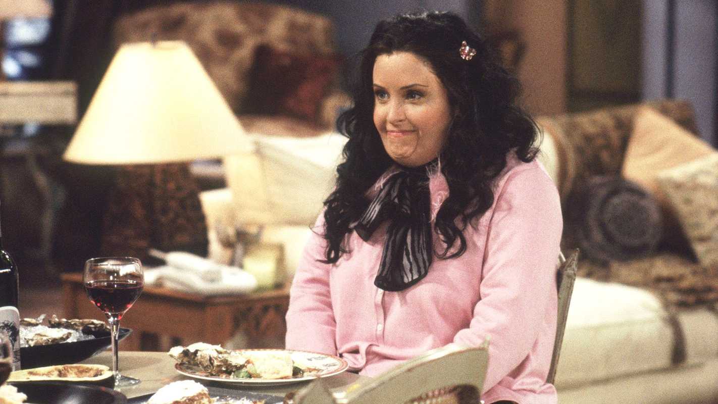Courteny Cox wearing a fat suit and sitting at the dinner table as Fat Monica in Friends.
