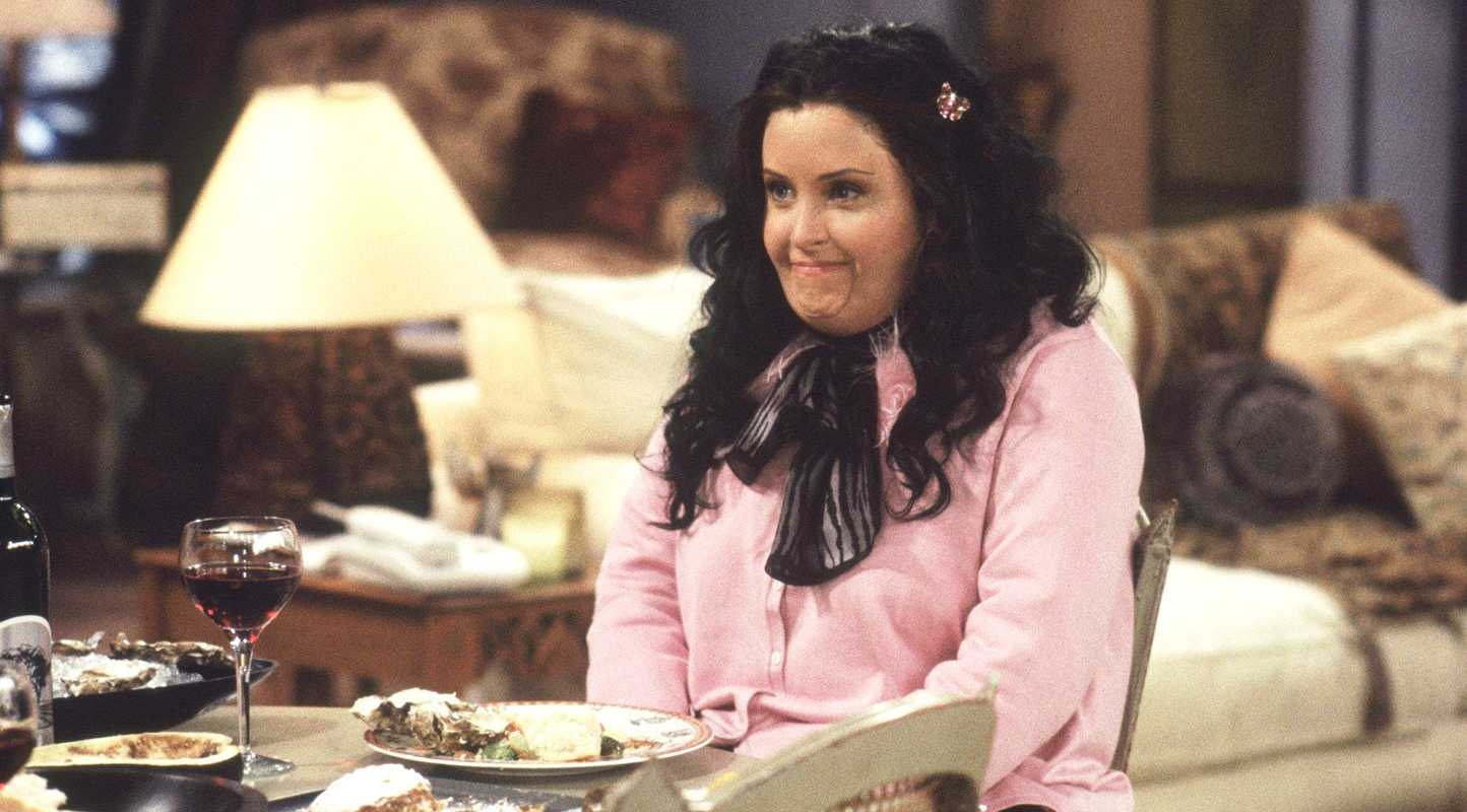 Courteny Cox wearing a fat suit and sitting at the dinner table as Fat Monica in Friends.