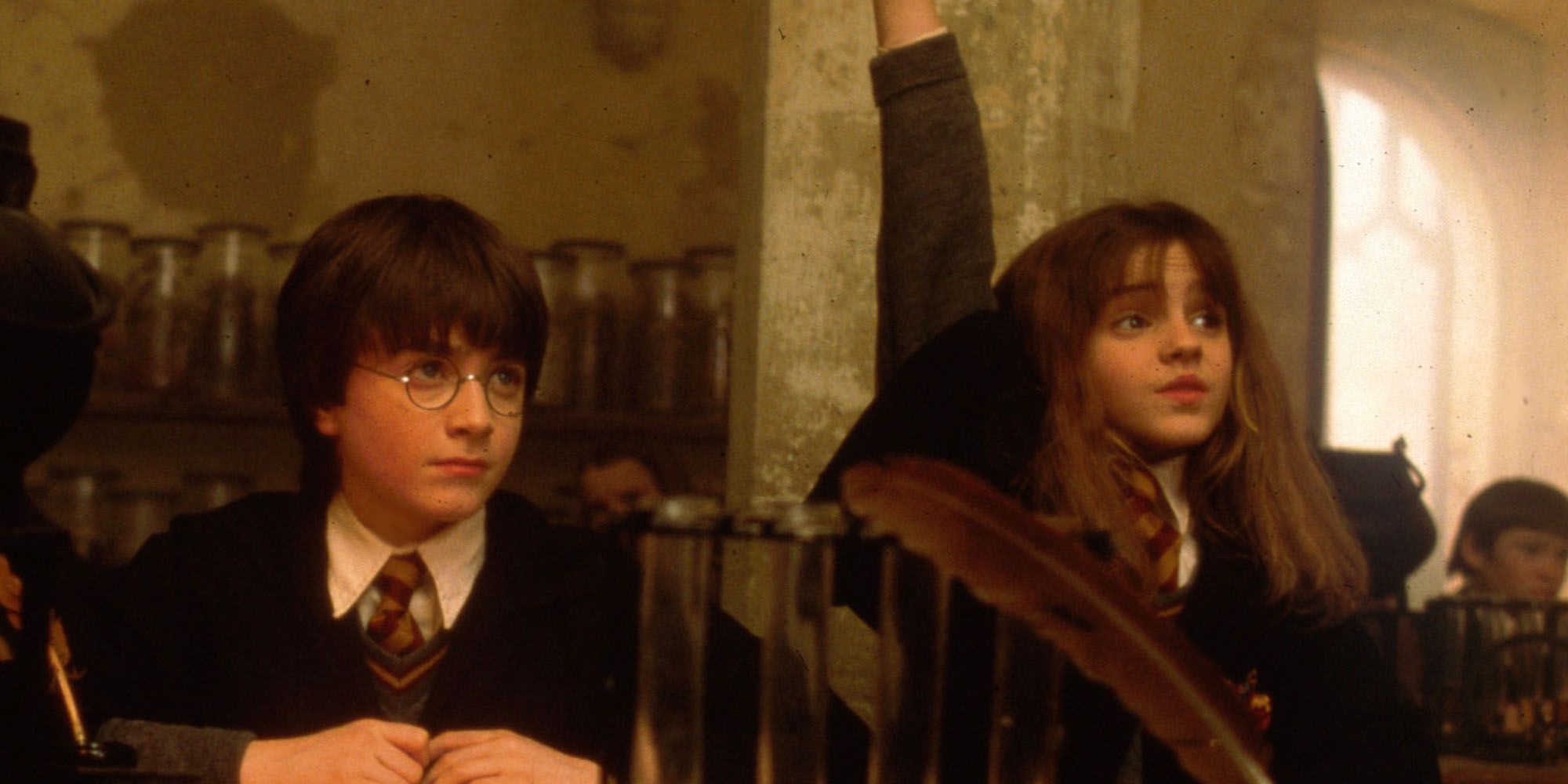 Daniel Radcliffe as a sullen Harry Potter and Emma Watson as an eager Hermione Granger, raising her hand, in Potions class in Harry Potter and the Sorcerer's Stone