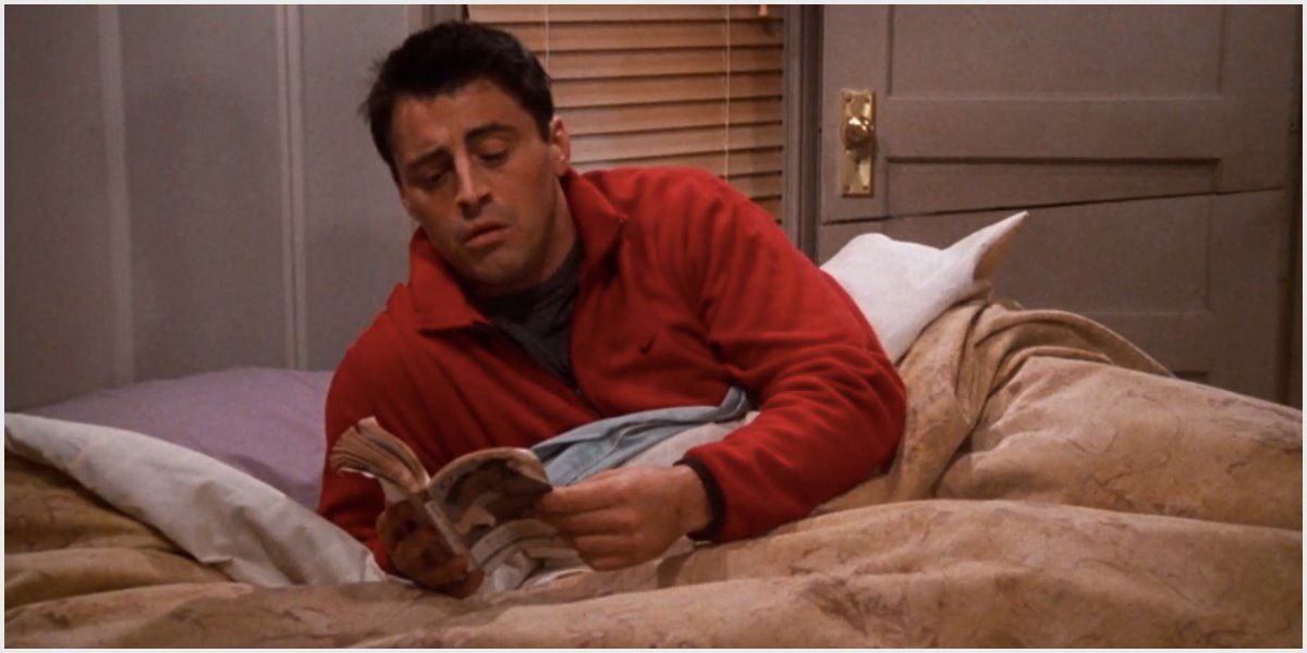 Joey na cama segurando um livro sobre Friends