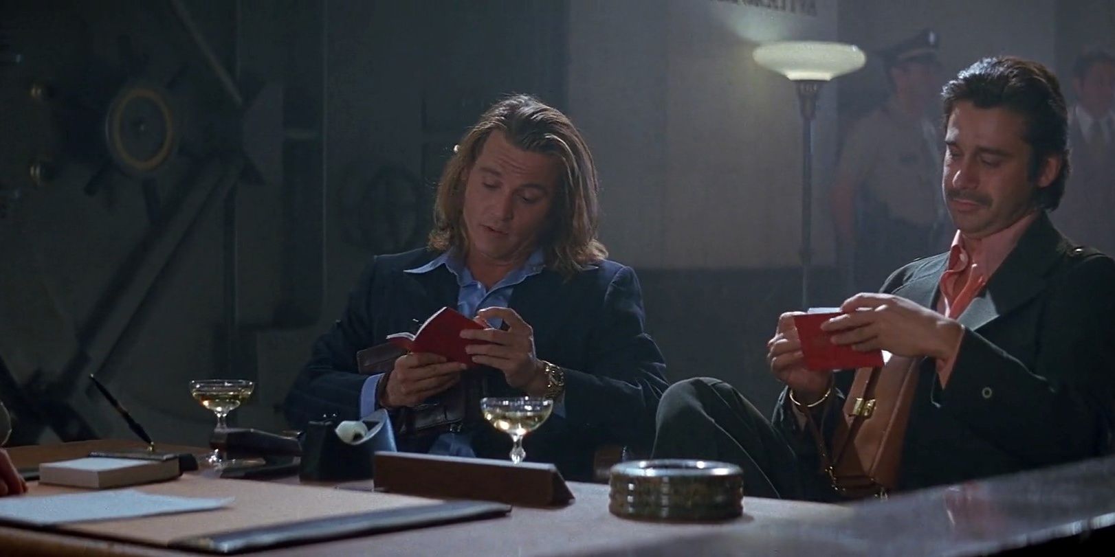 Two characters looking at passports and drinking champagne in Blow