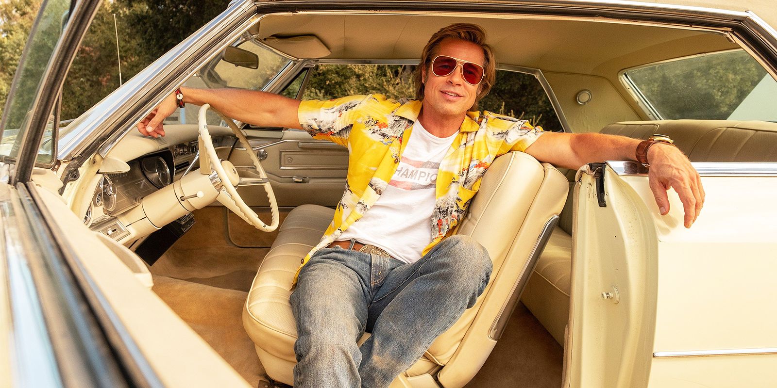 Brad Pitt como Cliff Booth sentado em seu carro com a porta aberta em Era uma vez em Hollywood