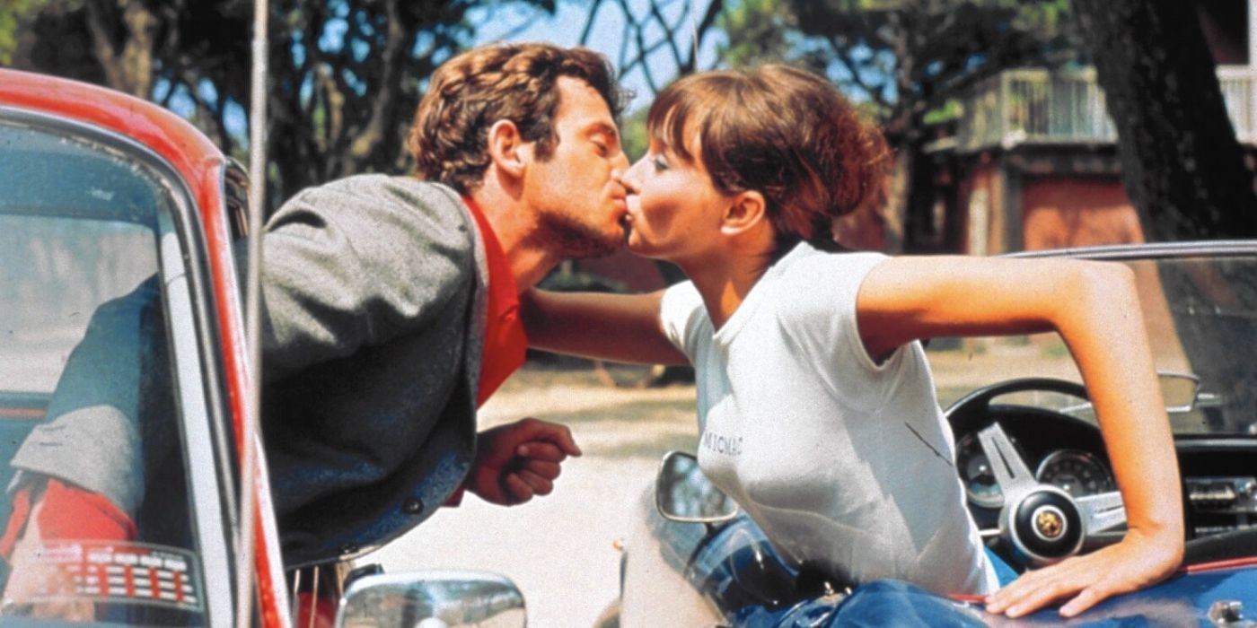 A man and a woman kiss through a car in Pierrot Le Fou (1965).