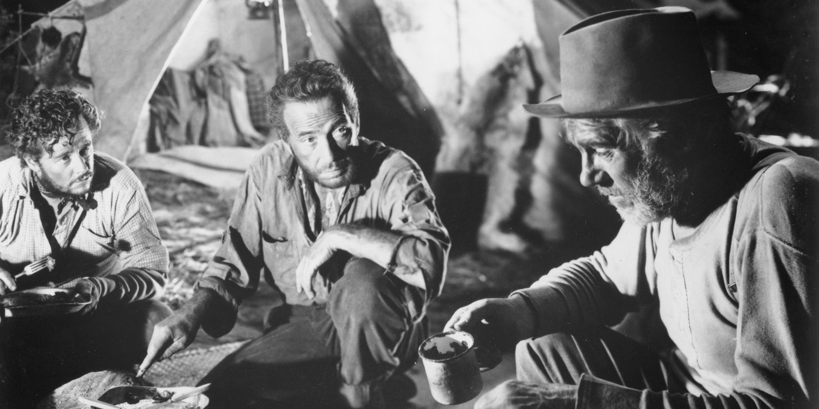 Three men sitting inside a tent and looking serious in The Treasure of Sierra Madre