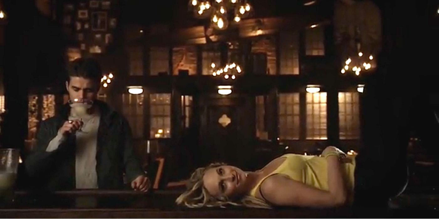 Caroline se deita em um bar enquanto Stefan bebe atrás dela em The Vampire Diaries