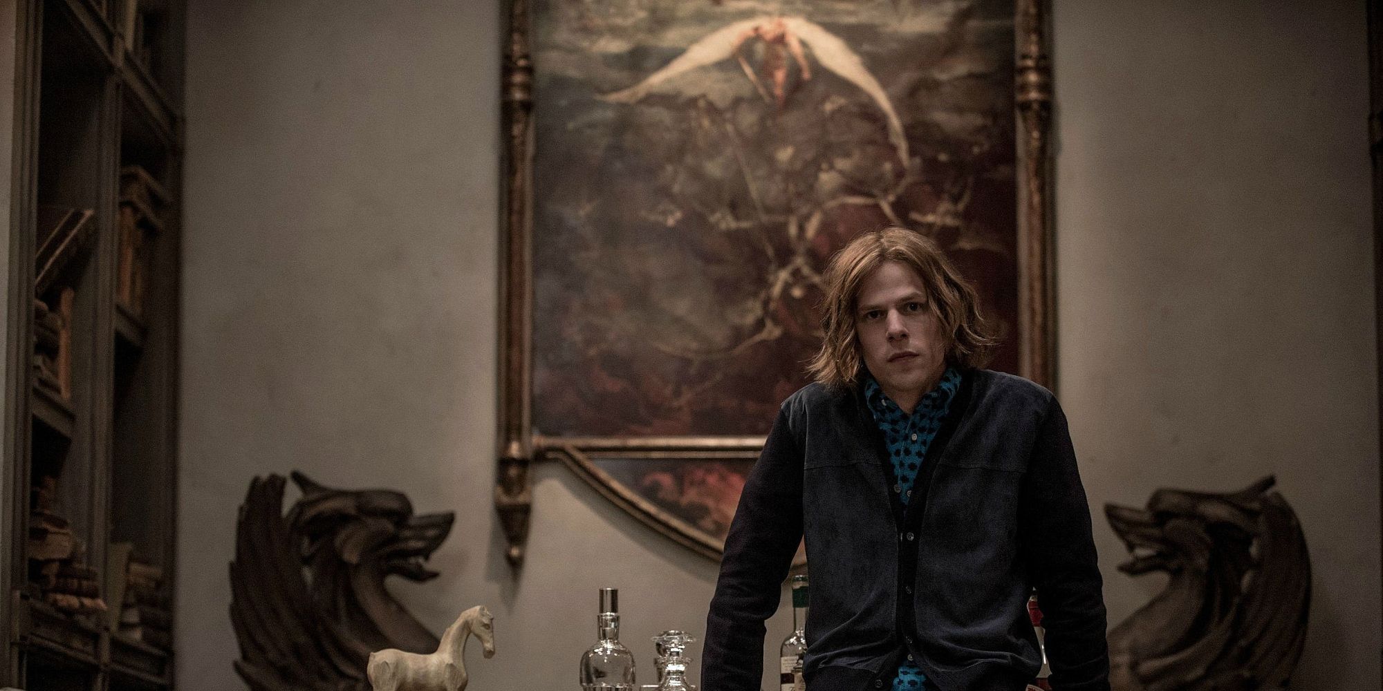 Lex Luthor sitting on his desk by his painting of angels and demons in Batman v Superman