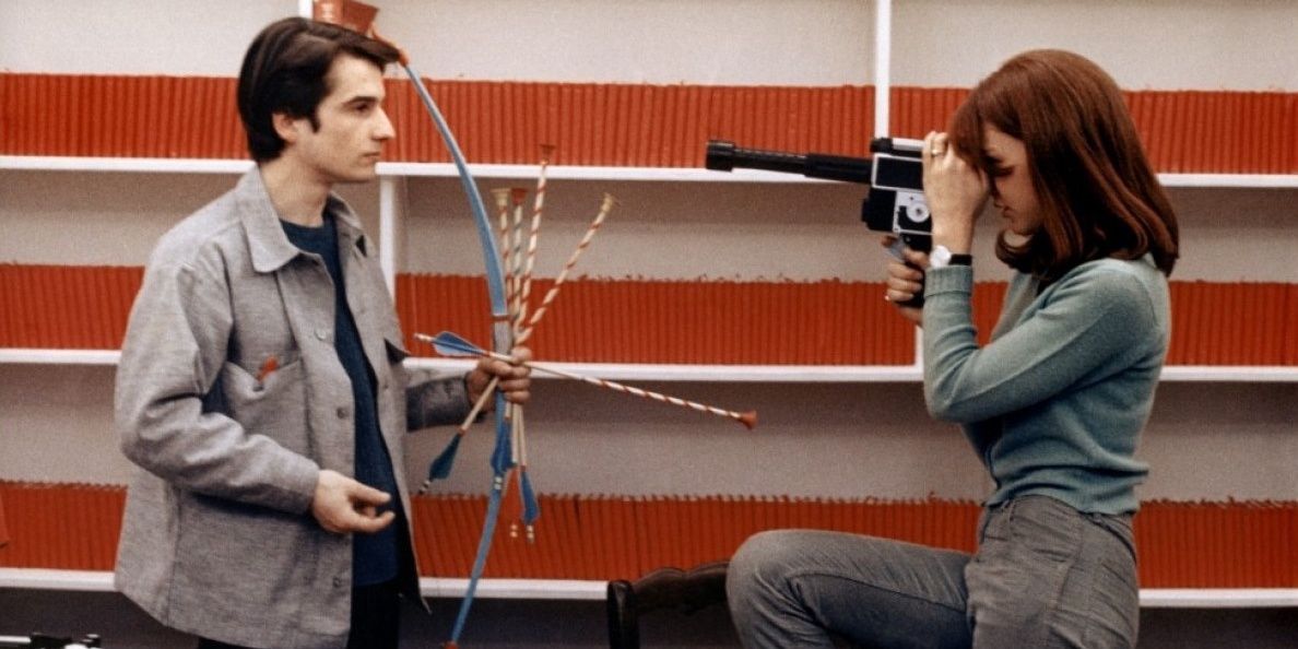 A woman records a man holding a bow and arrows in La Chinoise.