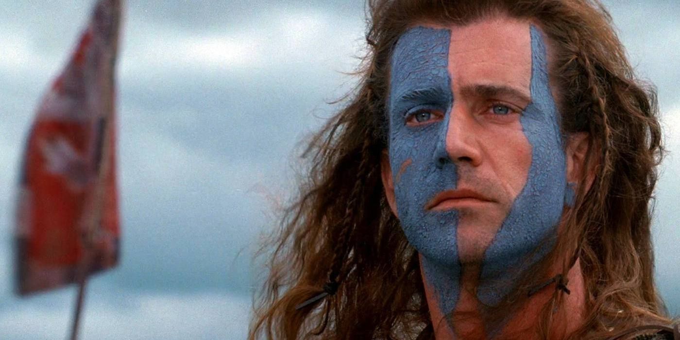 Un primer plano de Mel Gibson mientras mira solemnemente a lo lejos con el rostro pintado de azul.
