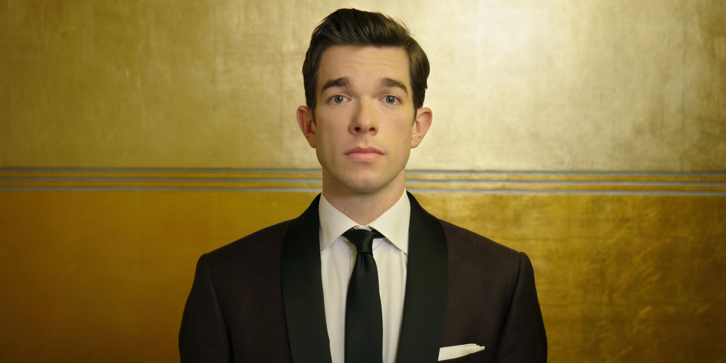 John Mulaney stares at the camera with a yellow background