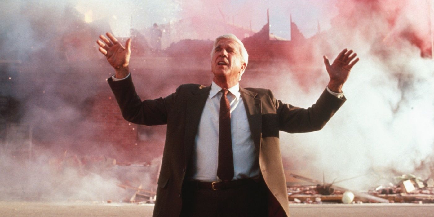 Leslie Nielsen as Frank Drebin waving his arms in front of a large explosion in The Naked Gun