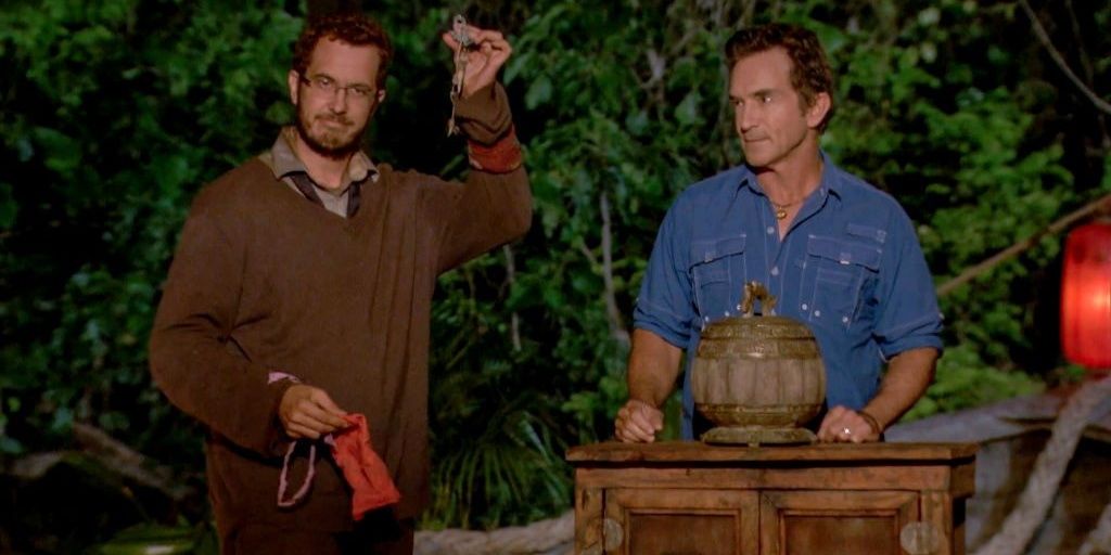 Rick Devens holding up an idol at tribal council standing next to Jeff Probst in Survivor: Edge Of Extinction