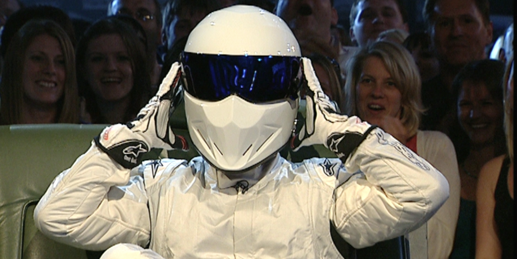 The Stig preparing to take off their helmet on the couch on Top Gear