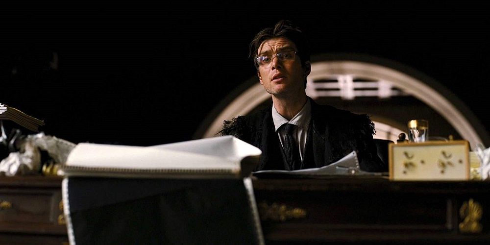 Cillian Murphy reads papers aloud at a desk in The Dark Knight