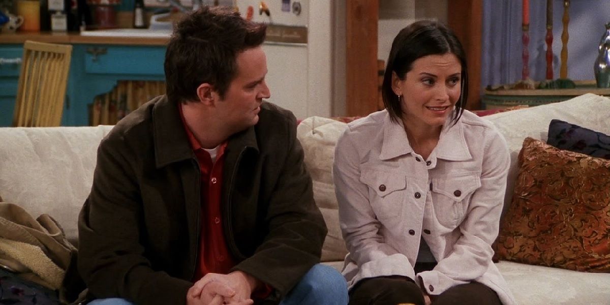 Monica grimacing while sitting next to Chandler on her and Rachel's couch