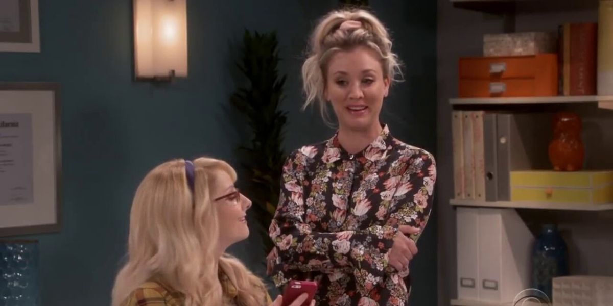 Penny in a floral top standing over Bernadette who is looking up at her