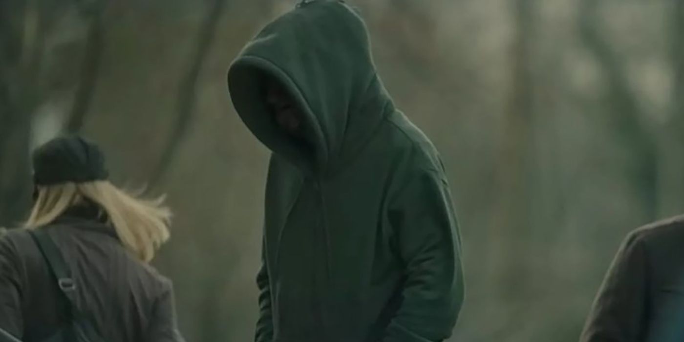 A man or entity wearing a hoodie over their face, standing to the left in a scene from The Outsider.