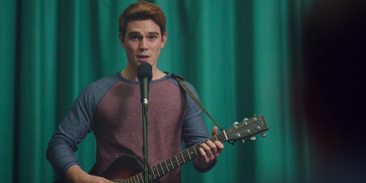Archie playing his guitar in front of green curtain in Riverdale