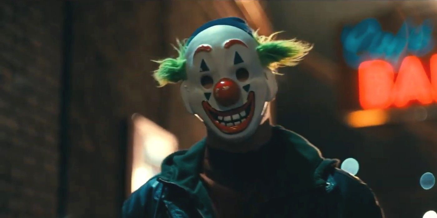 A thug in a clown mask holds up the Wayne family in an alley in Joker