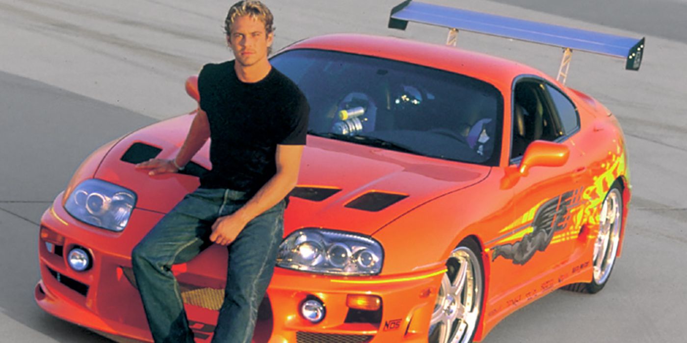 Brian O'Connor posing next to a red car in The Fast and the Furious.