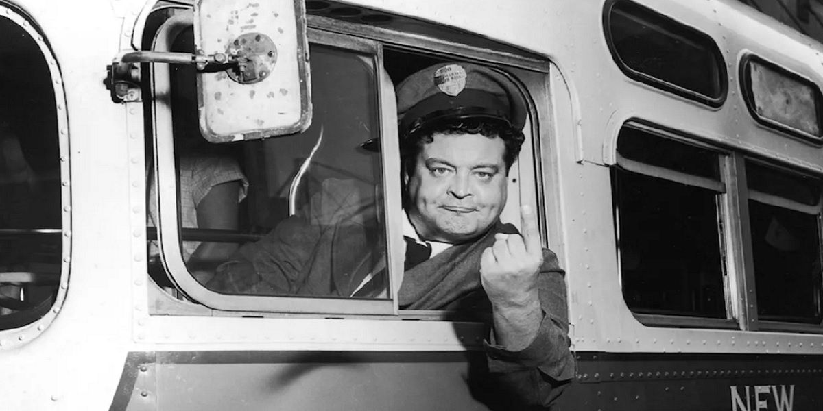 Jackie Gleason as Ralph Kramden, angrily pointing his finger out the window of a bus