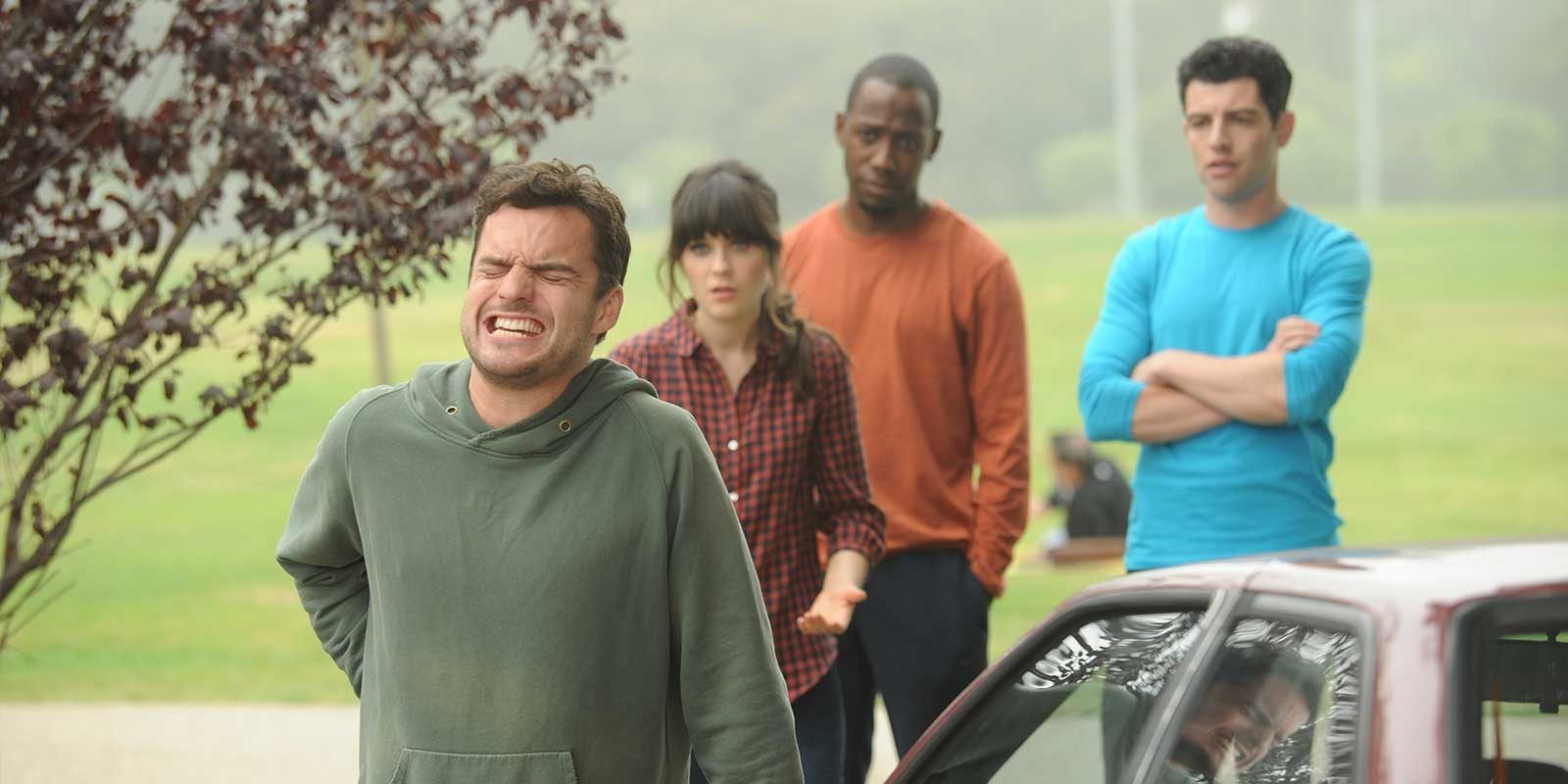 Nick grimaces in pain while his roomates watch him in New Girl