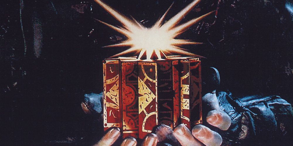 A pair of hands holds the Lament Configuration, the puzzle box from the Hellraiser franchise. A burst of light appears above it.