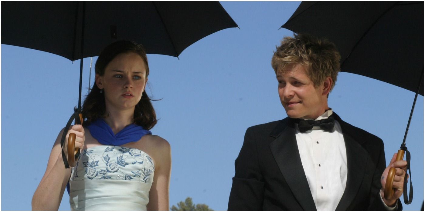 Rory and Logan in formalwear, outside on a sunny day, holding black umbrellas