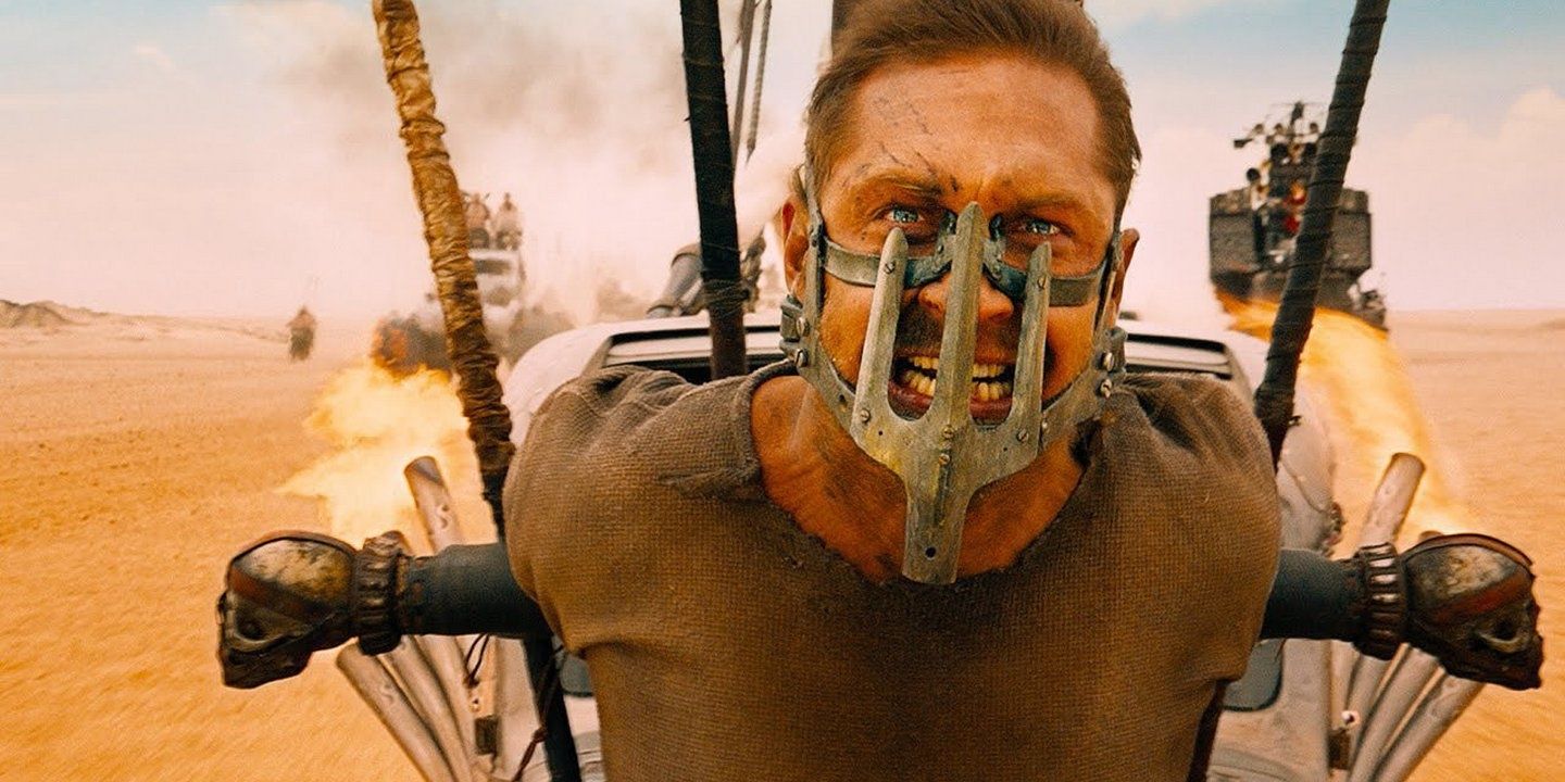 Tom Hardy in Mad Max Fury Road chained to the front of a car screaming wearing a mouth grill 