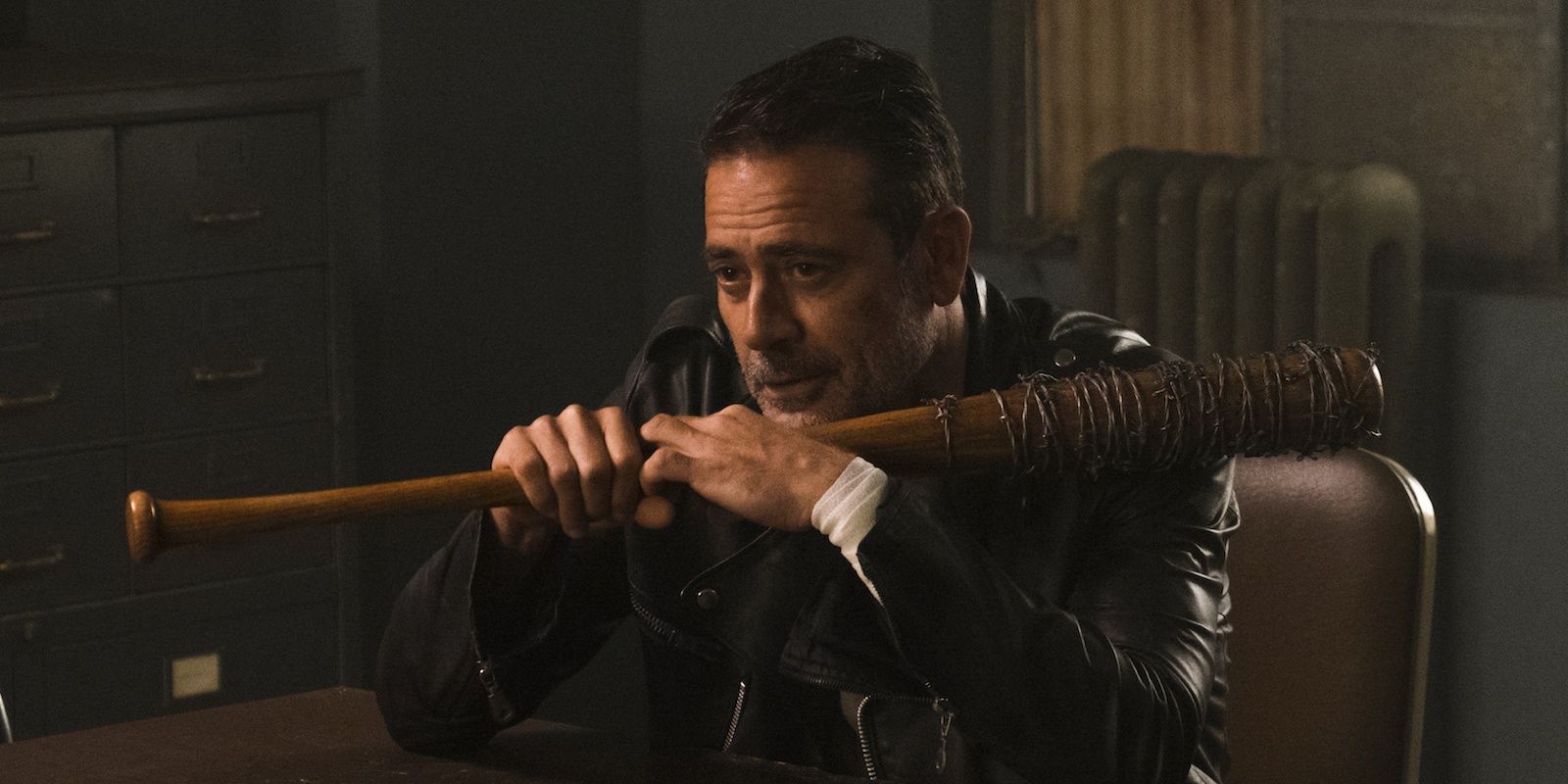 Negan sitting in a chair holding Lucille in Walking Dead.